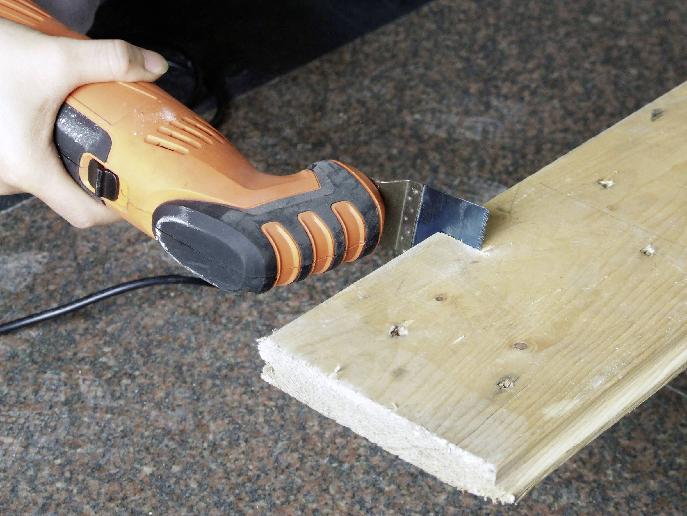 Una persona taglia un tavola di legno con un utensile elettrico arancione su una superficie di granito.