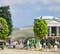 Persone in un cimitero in miniatura con lapidi, alberi e innaffiatoi. Sullo sfondo è visibile un edificio templare e il paesaggio.