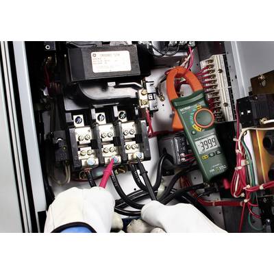 Mani con guanti protettivi misurano la tensione elettrica in un quadro elettrico utilizzando un multimetro. Il display mostra -3999.