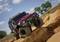 Un fuoristrada rosso percorre un terreno off-road roccioso sotto un cielo blu con nuvole bianche. Sullo sfondo sono visibili degli alberi.