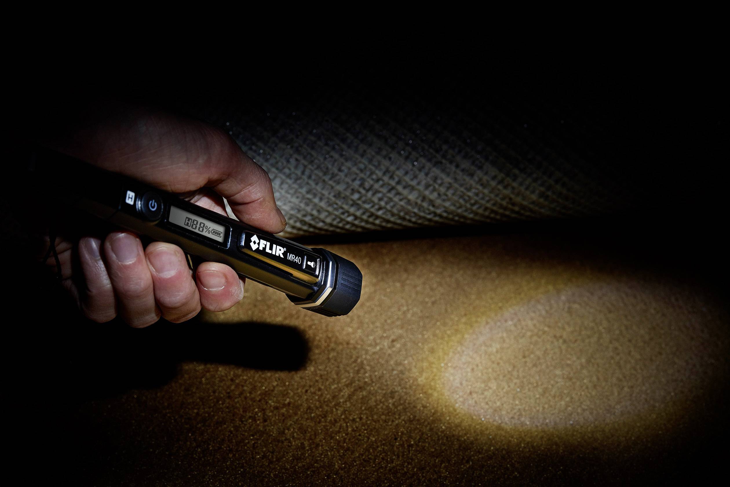 Una mano tiene una torcia che illumina il pavimento. Il fascio di luce evidenzia l'area sotto un tappeto sollevato.