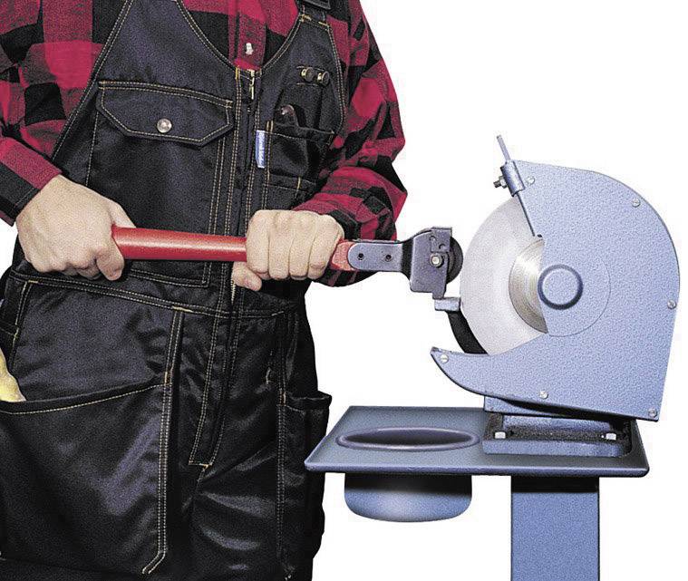 Persona in abbigliamento da lavoro che leviga un utensile su una smerigliatrice da banco.