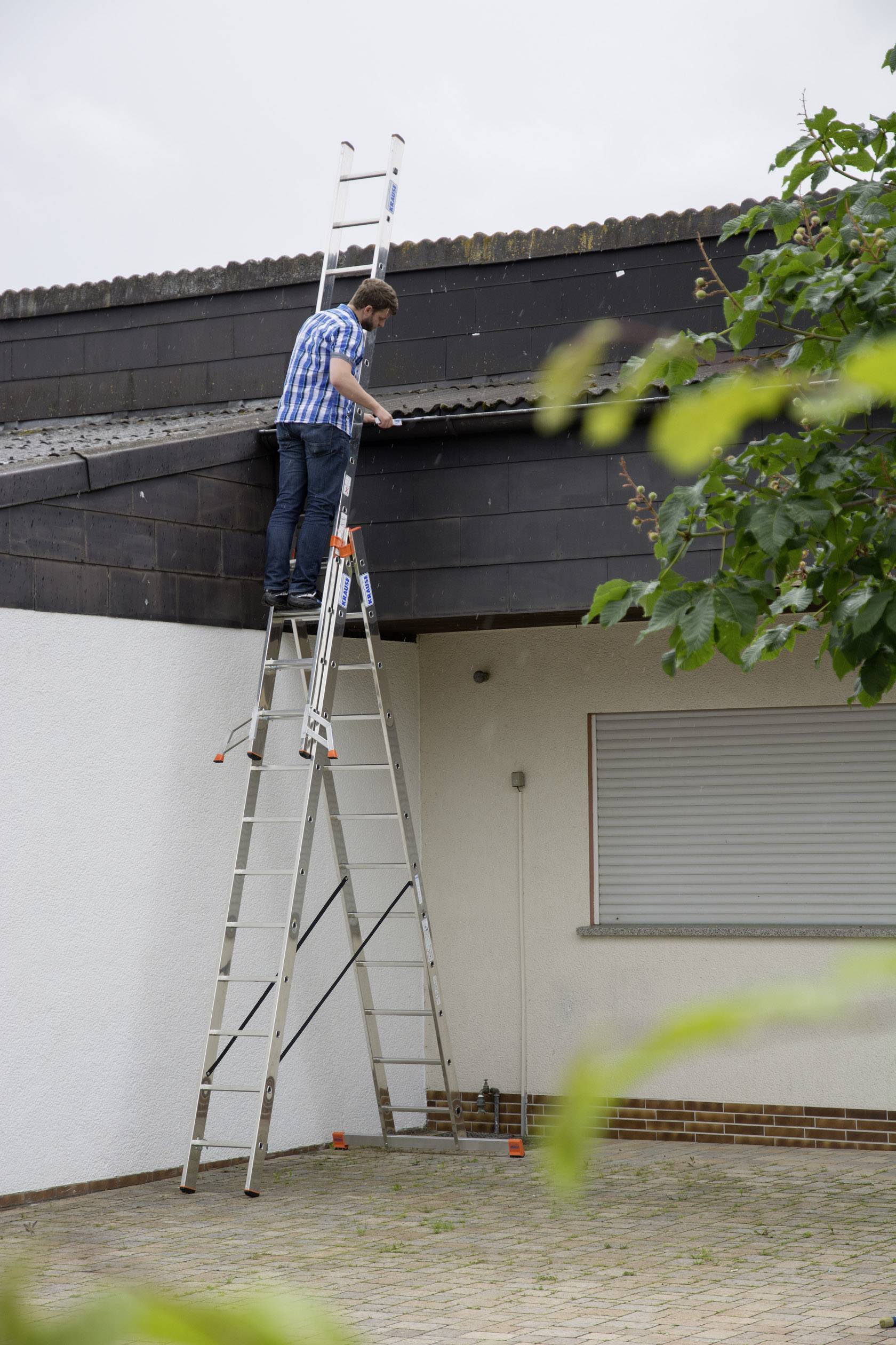 Un uomo è in piedi su una scala alta, appoggiata a una casa. Sta lavorando sul tetto o sulla grondaia della casa.