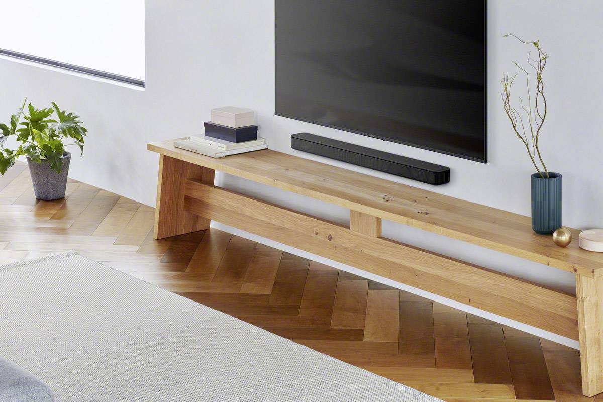 Un soggiorno moderno con un mobile TV in legno. Sopra ci sono libri, un altoparlante e piante. Sulla parete è appeso un grande televisore.
