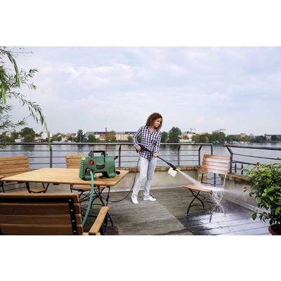 Una donna sta pulendo una terrazza con un'idropulitrice, con mobili in legno. Sullo sfondo è visibile un fiume con una vista della città.