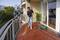 Un uomo sta pulendo un balcone con un idropulitrice. La terrazza ha piastrelle rosse, e sullo sfondo si vedono piante e edifici.