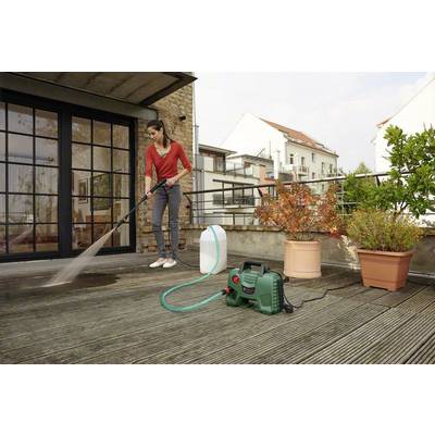 Una persona sta pulendo una terrazza con un idropulitrice. Sullo sfondo sono visibili piante e edifici.