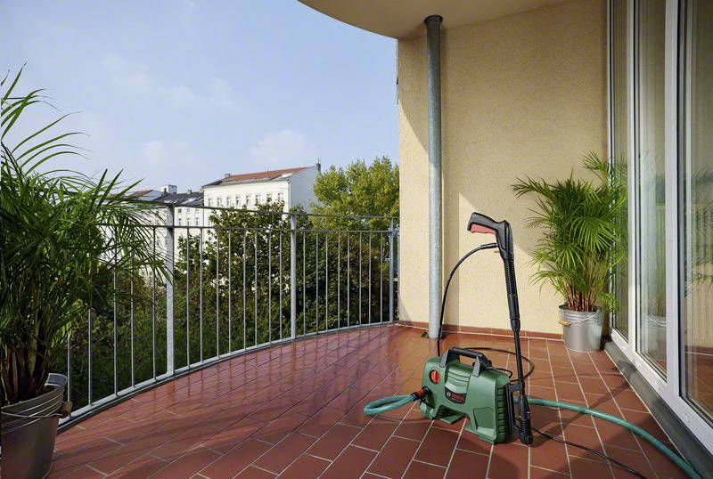 'Idropulitrice verde su un balcone con vista su edifici e alberi. A sinistra e a destra ci sono piante in vaso.'