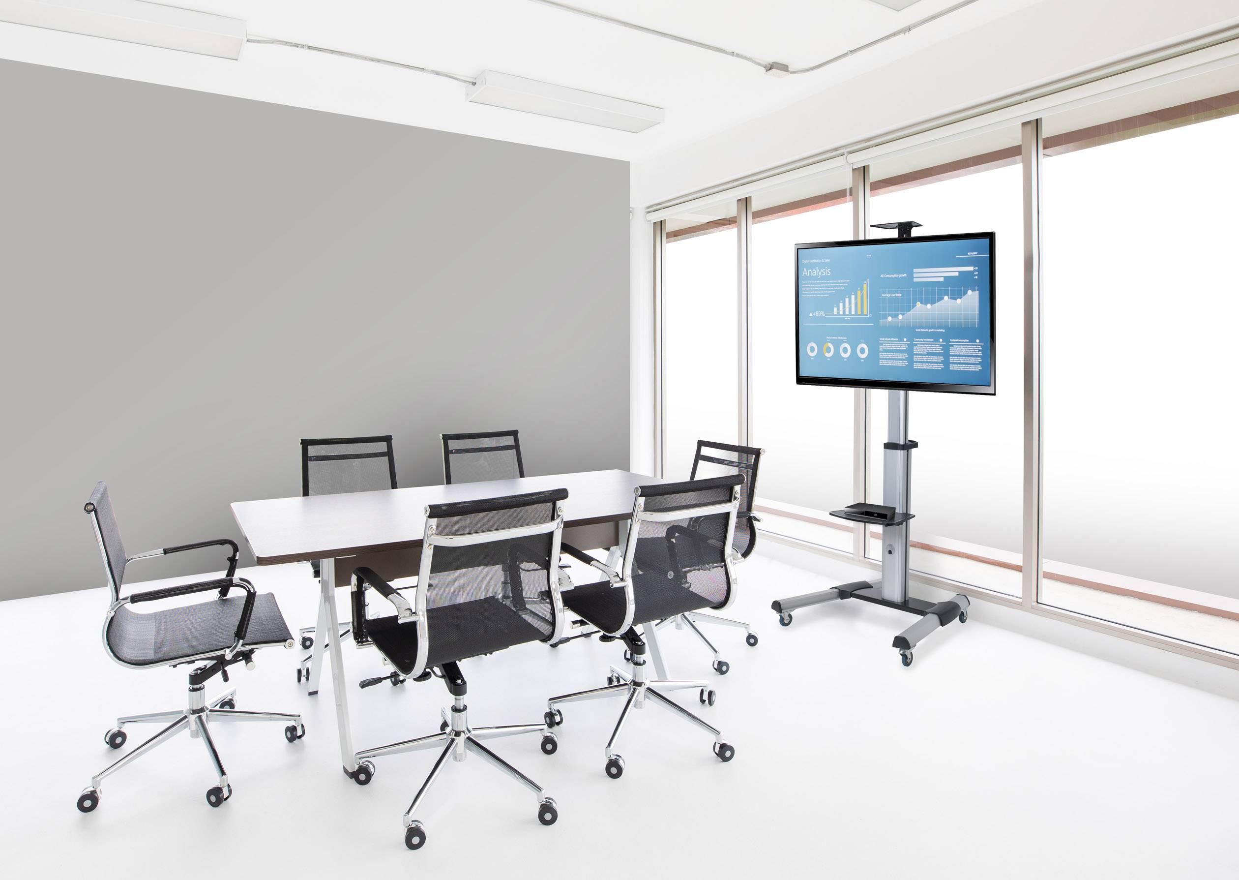 Sala conferenze con tavolo, sei sedie e schermo che mostra un diagramma con dati aziendali. Arredamento luminoso e moderno.