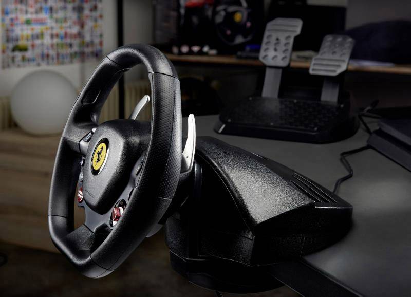 Controller del volante con logo Ferrari sul tavolo, due pedali sullo sfondo. Adatto per simulazioni di guida.