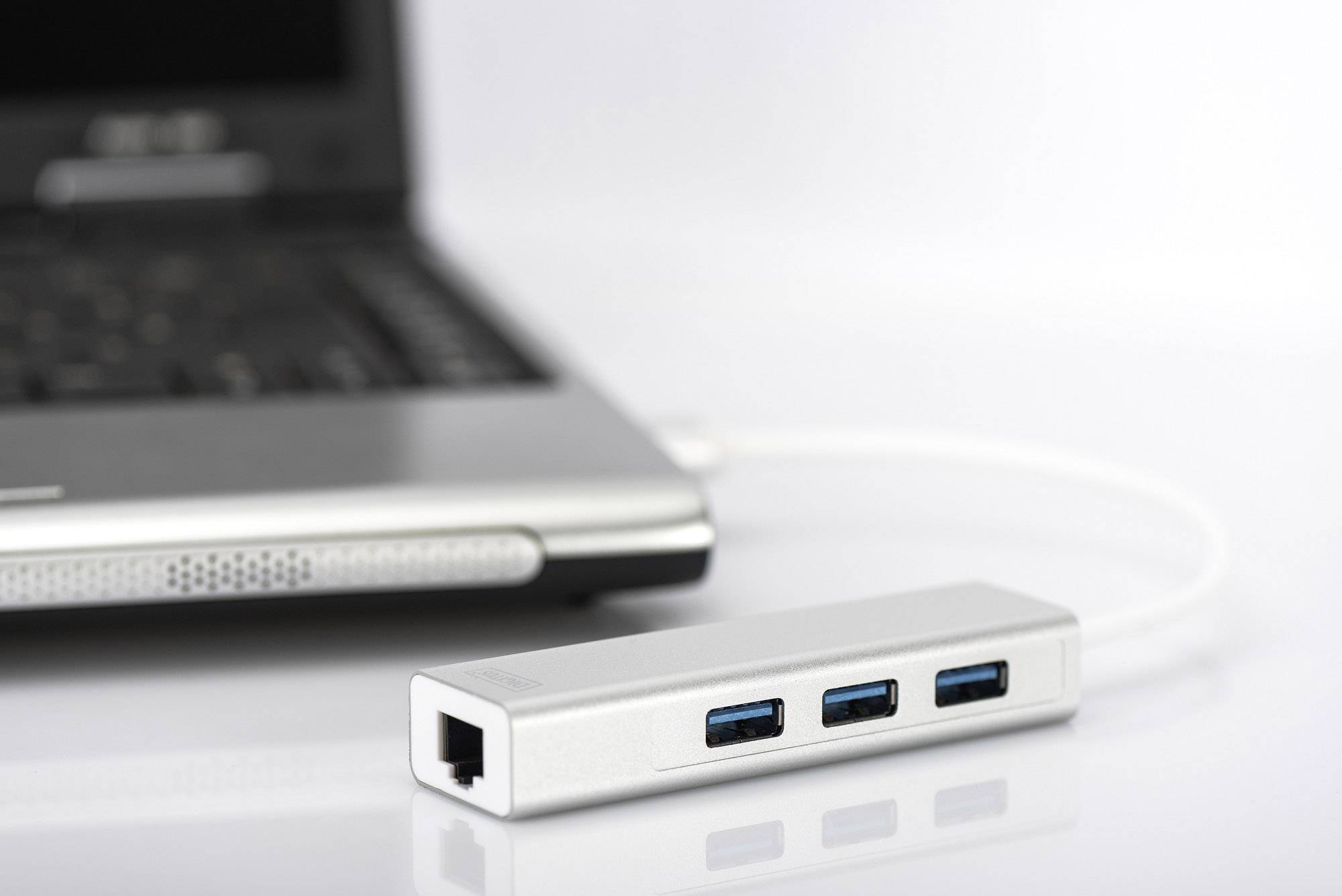 Hub USB argentato con tre porte USB 3.0 blu, collegato a un laptop aperto su uno sfondo bianco.