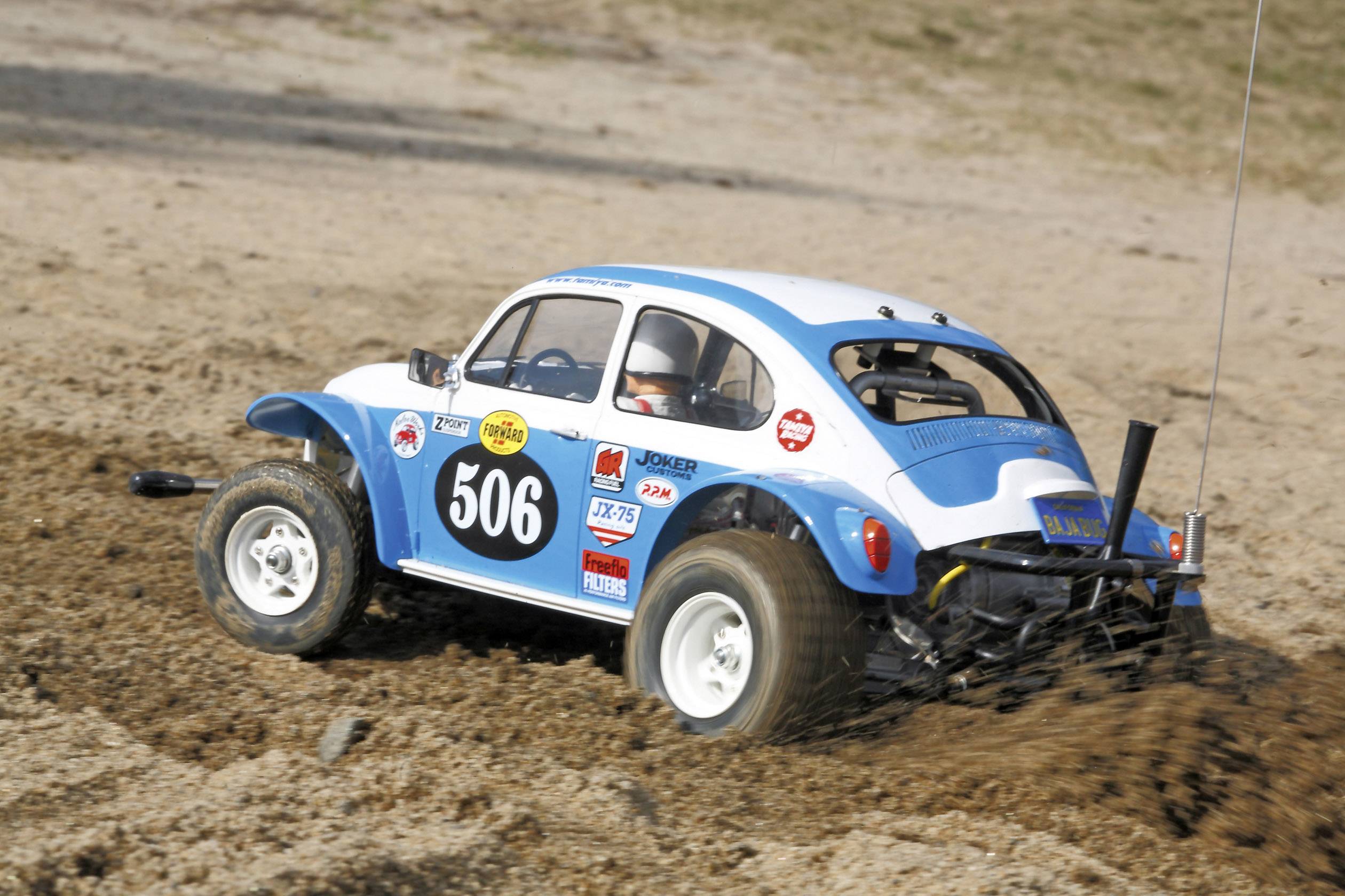 Un buggy telecomandato blu e bianco guida su un terreno sabbioso. Il numero '506' è visibile sul lato.