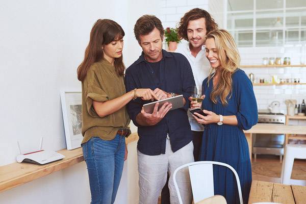 Un gruppo di quattro persone è in piedi in un ufficio moderno e sta osservando insieme un tablet. Sembrano concentrati e interessati.