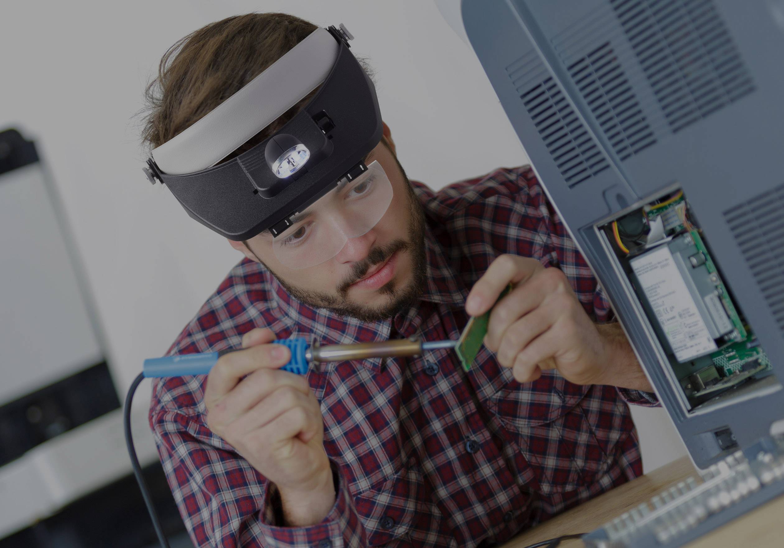 Un uomo salda con concentrazione su una scheda elettronica all'interno di un case per computer. Indossa occhiali protettivi e una lente d'ingrandimento.