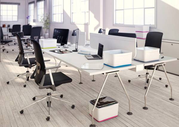 Un moderno ufficio open space con diverse scrivanie, sedie e laptop. La luce del sole entra attraverso ampie finestre.
