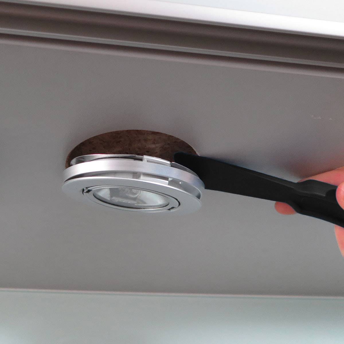 Una persona rimuove un LED rotondo da un supporto a soffitto utilizzando un utensile piatto.