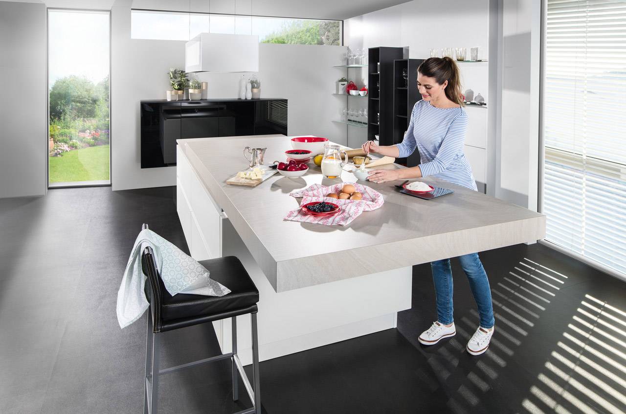 Una donna sta preparando la colazione in una cucina moderna con una grande vista finestrata. Sul piano di lavoro ci sono pane, uova e succo.