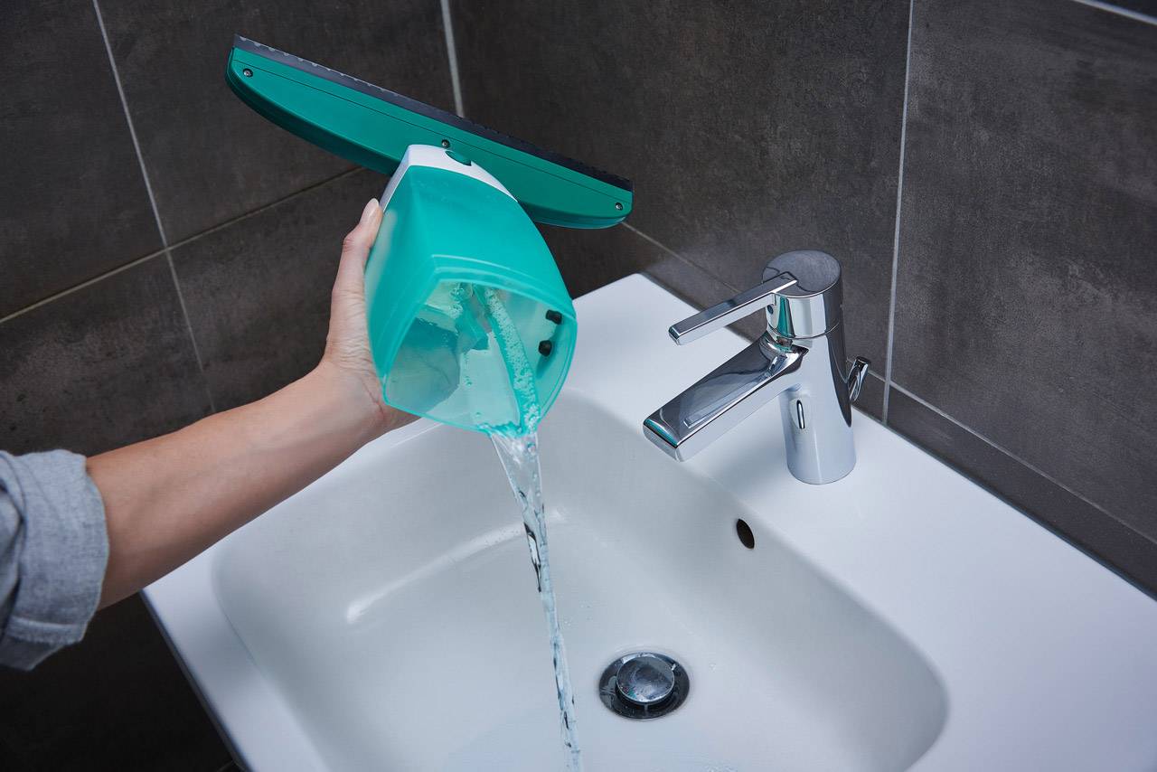 Una mano versa l'acqua da un secchio per lavapavimenti in un lavandino, accanto a un rubinetto.