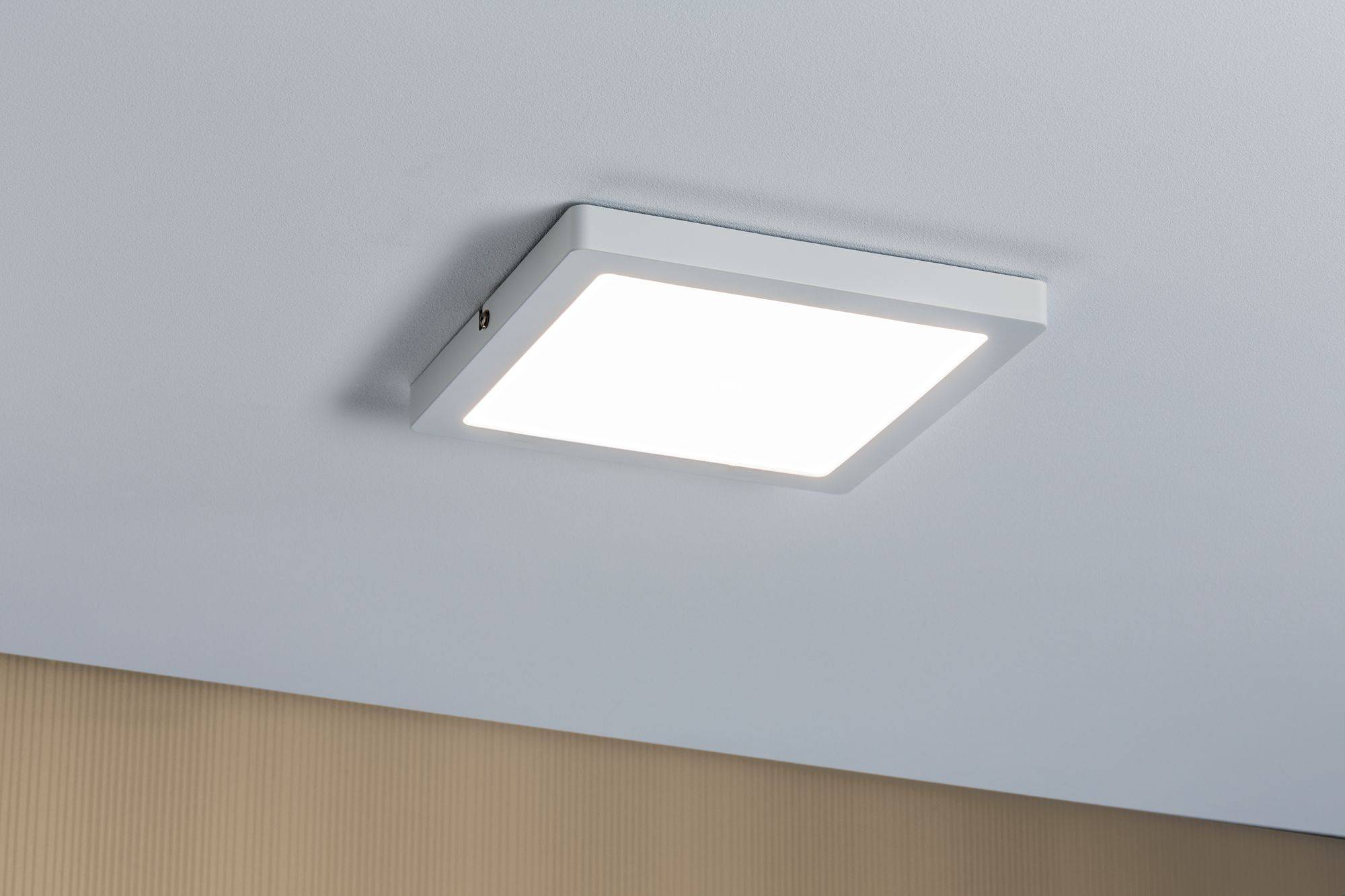 Plafoniera quadrata e piatta con cornice bianca, montata su un soffitto chiaro sopra una parete beige.