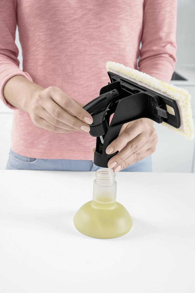 Una persona con un maglione rosa sta riempiendo una bottiglia spray con un liquido giallo.
