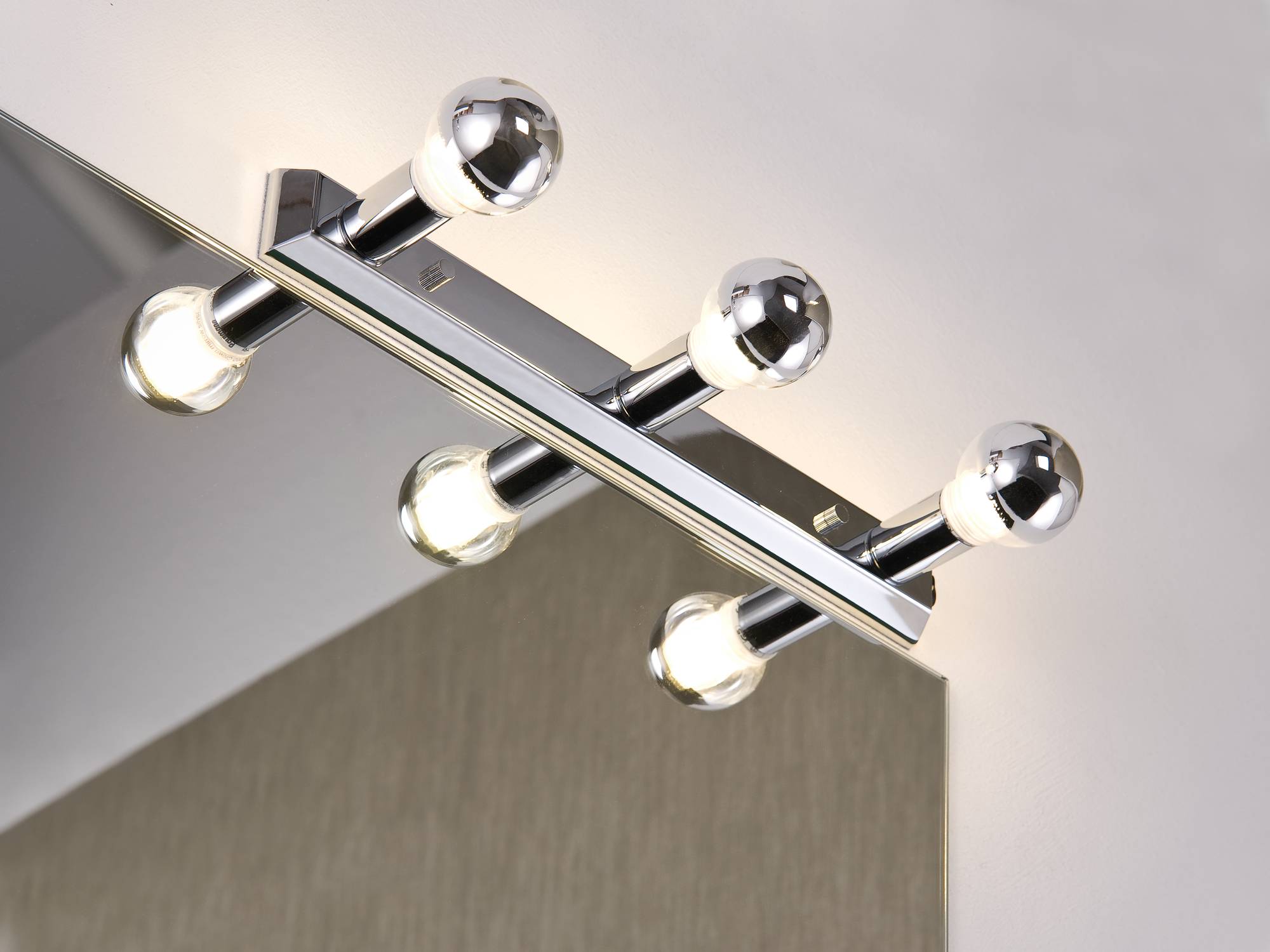Tre lampadine sferiche su supporto cromato, illuminate, montate a parete. Design moderno, illuminazione uniforme.