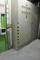 Grande armadio elettrico con segnali di avvertimento e spie di controllo in un ambiente industriale, circondato da parete verde e documenti.