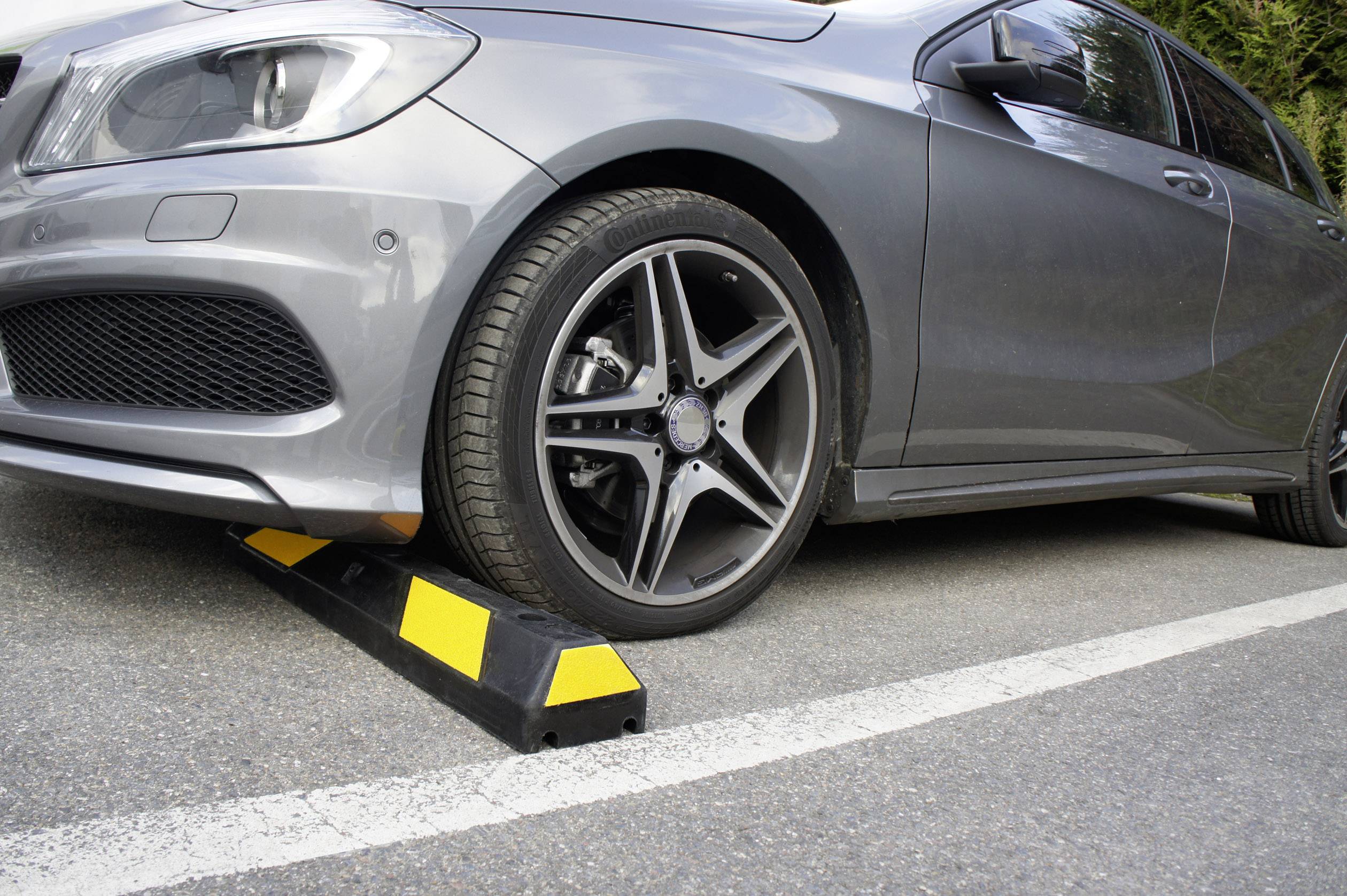 Un'auto grigia attraversa un dosso giallo e nero su un parcheggio asfaltato.