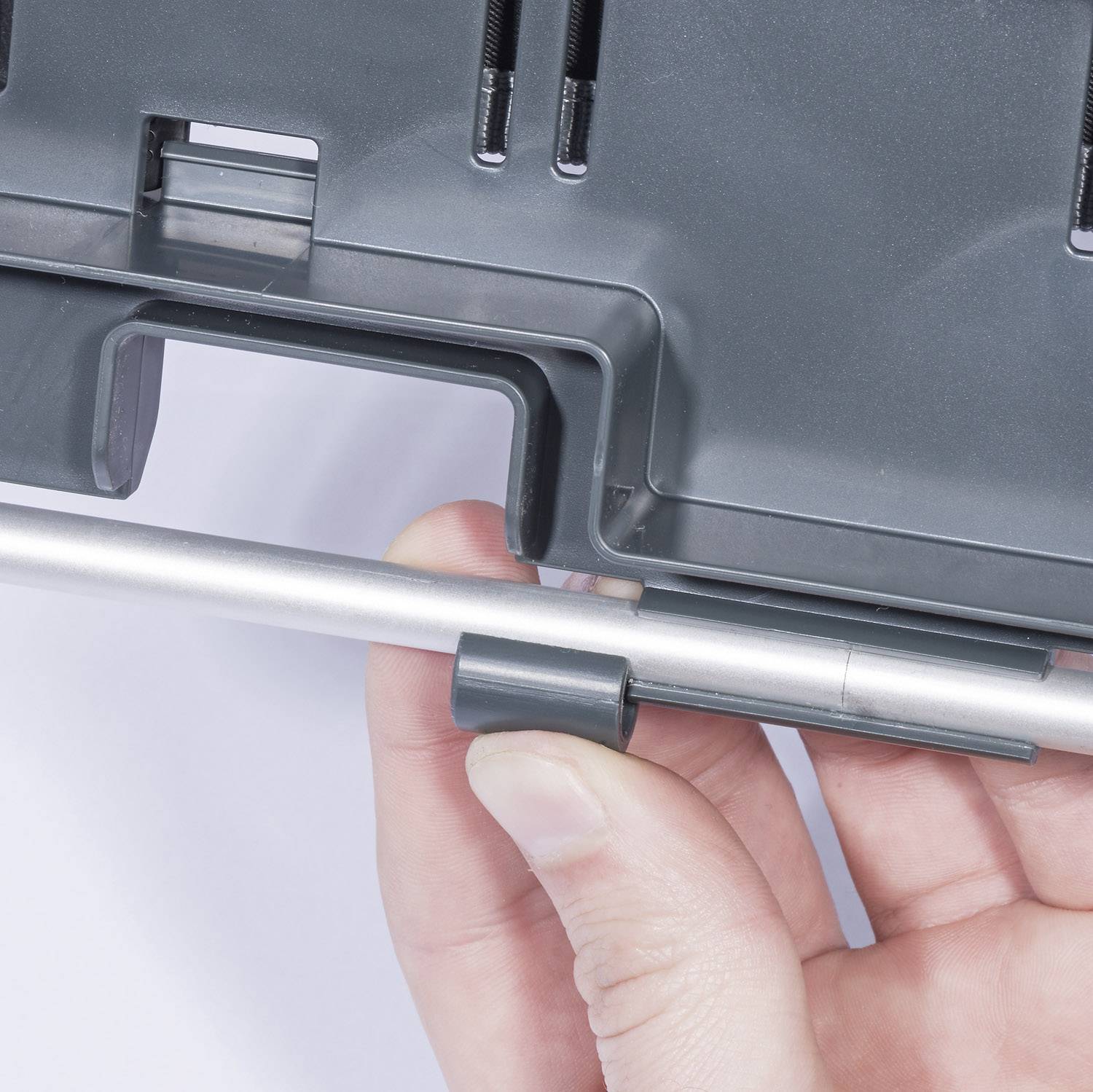 Una mano tiene un pezzo di plastica grigio con una barra metallica argentata inserita in un supporto.