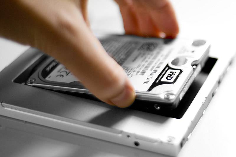 Una mano installa un hard disk in un laptop. L'hard disk viene tenuto vicino all'apertura dello slot per hard disk.
