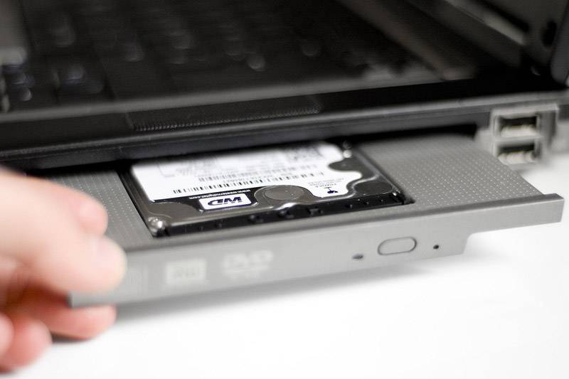 Una mano sta estraendo parzialmente un disco rigido rimovibile da un laptop. Il disco rigido è trattenuto da un alloggiamento.