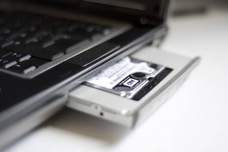 Un laptop con un disco rigido parzialmente estratto nello slot del lettore DVD. Il focus è sul disco rigido, che è stato modificato e inserito in modo non convenzionale.