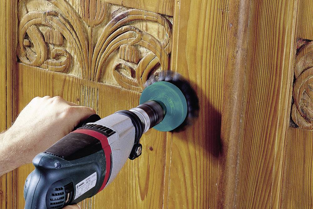 Una persona sta usando una levigatrice su una superficie di legno con intagli decorativi.