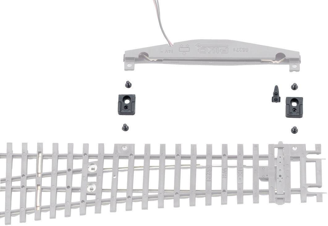 Tratto di binario con deviatoio montabile e quattro piccoli componenti per il modellismo ferroviario. Sopra si trova una traversina grigia con cavi.