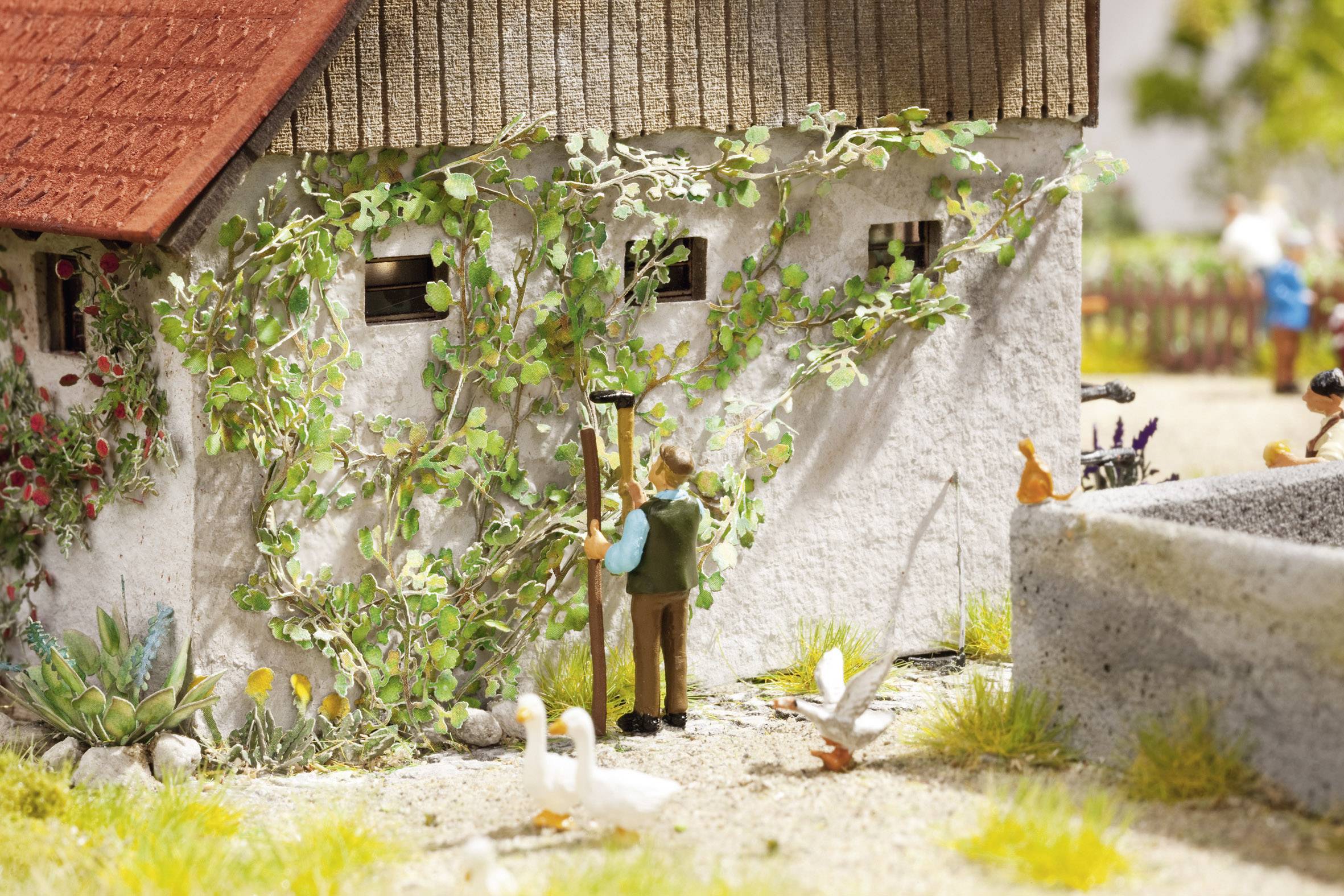 Un modellino in miniatura mostra una persona al lavoro in un edificio ricoperto di rampicanti, mentre alcune anatre passeggiano in primo piano.