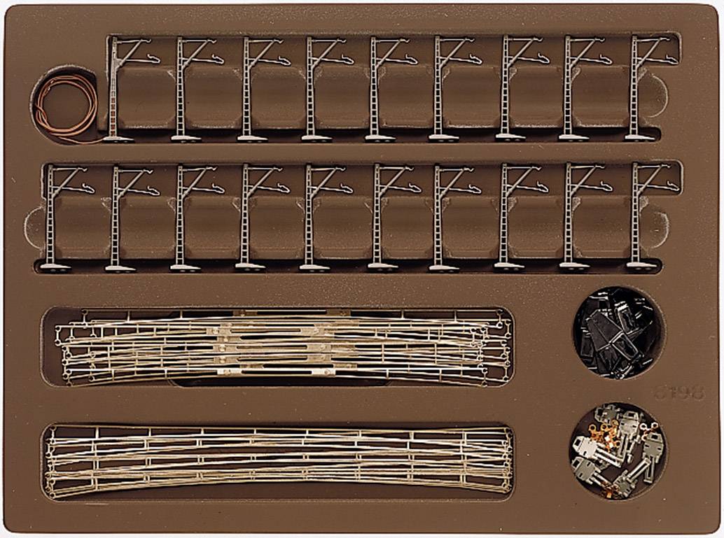 Un imballaggio con elementi di un set per modellismo ferroviario, inclusi pali della linea elettrica, binari e accessori, su sfondo marrone.