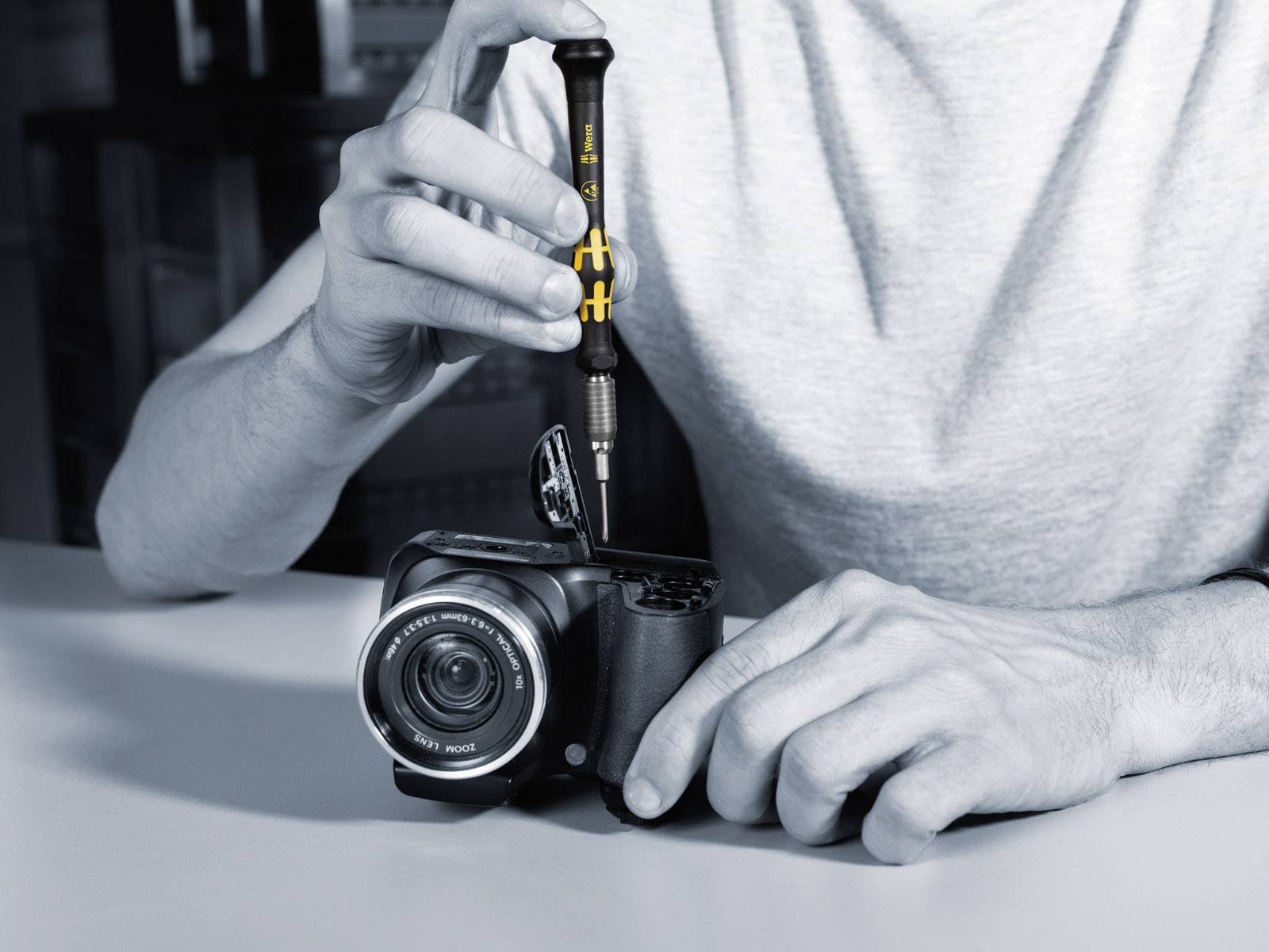 Una persona ripara una fotocamera con un cacciavite, rimuovendo il coperchio superiore.