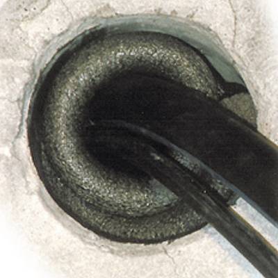 Primo piano di un cavo elettrico nero che attraversa un foro nel calcestruzzo. L'immagine si concentra sulla schermatura del cavo.
