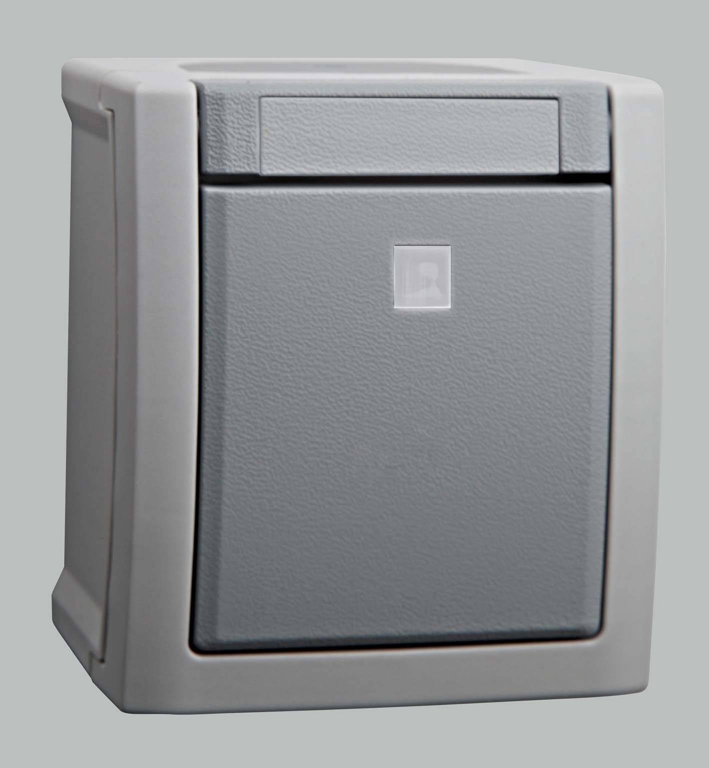 Un contenitore grigio rettangolare per fusibili con un piccolo simbolo quadrato al centro su uno sfondo grigio.