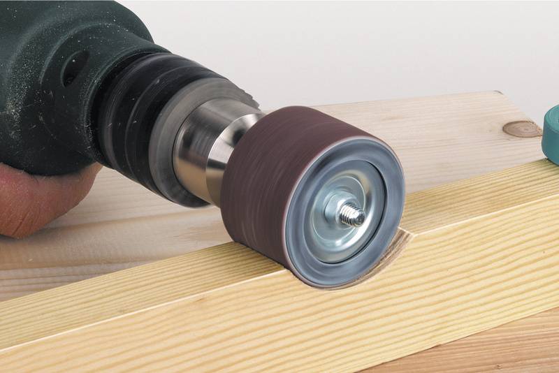 Trapano elettrico con accessorio per levigare liscia il bordo di una tavola di legno. La mano tiene il trapano in modo stabile.