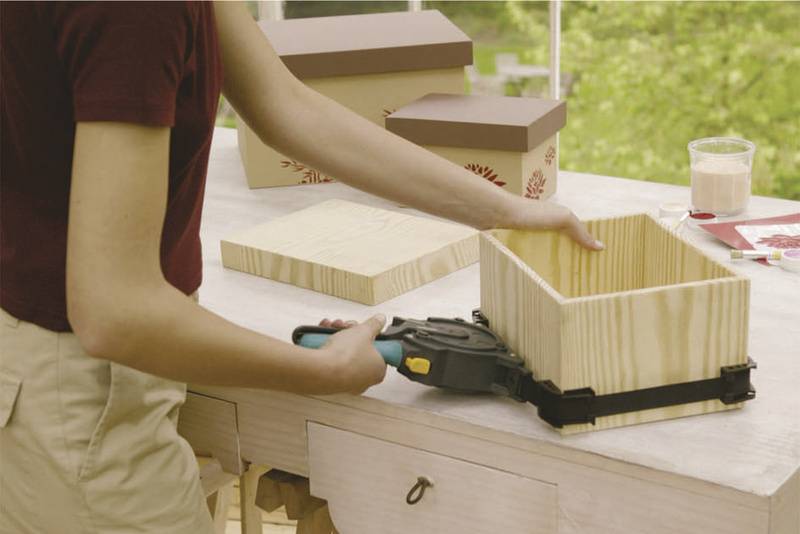 Una persona sta utilizzando un attrezzo di serraggio per assemblare una scatola di legno. Sul tavolo ci sono altri pezzi di legno e scatole.