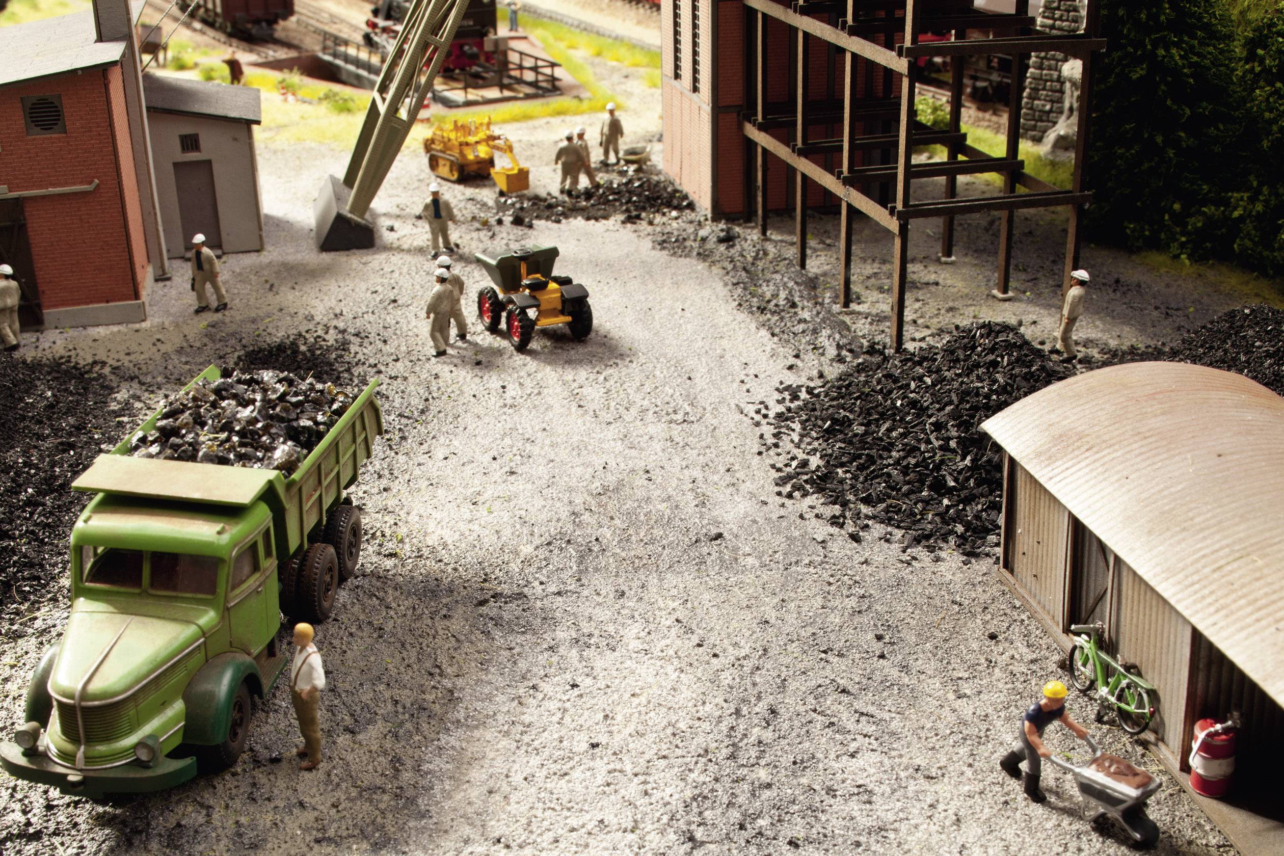 Una miniatura mostra operai intenti a caricare carbone su camion e macchine in un paesaggio industriale.