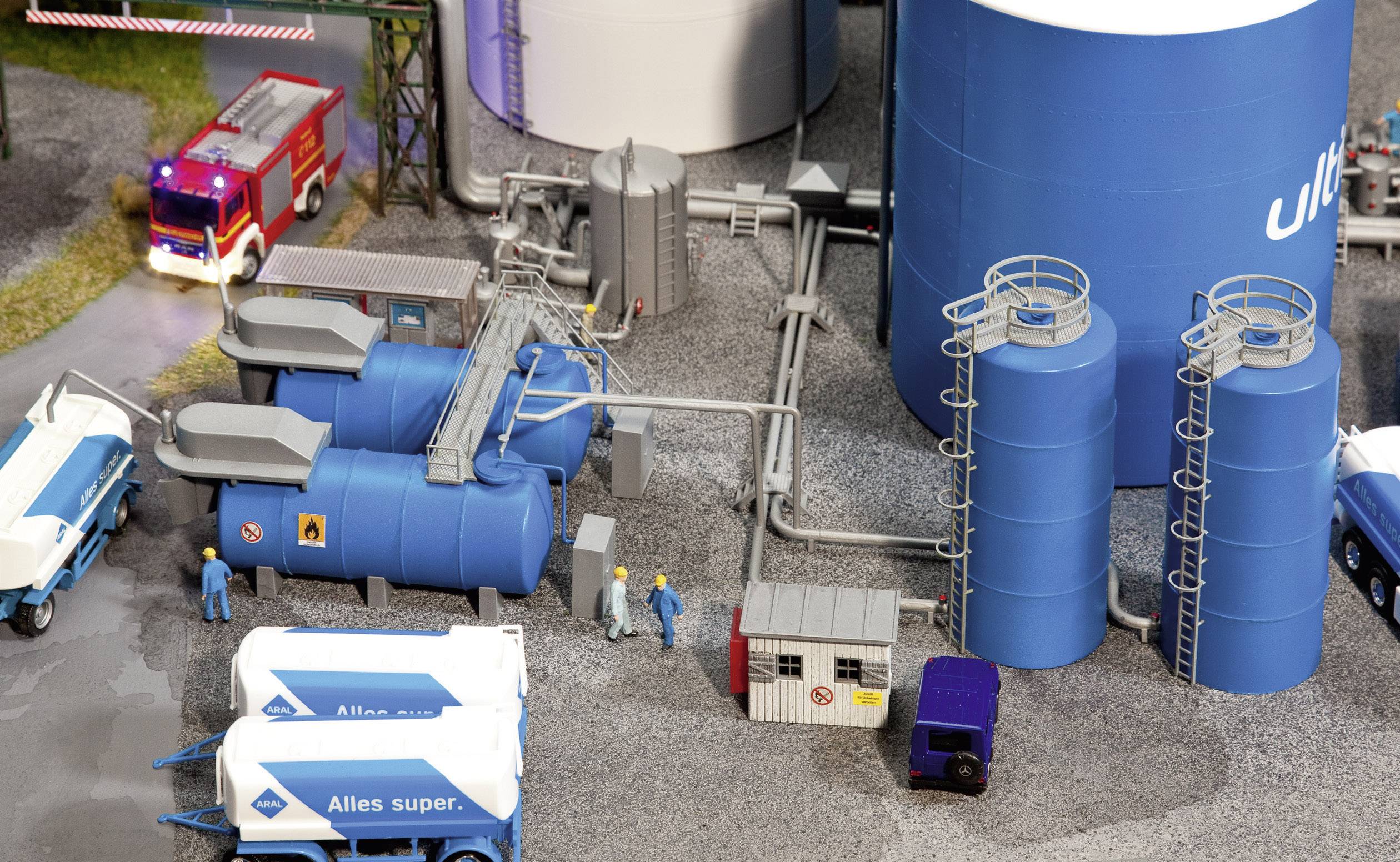 Un plastico in miniatura mostra una scena industriale con serbatoi blu, un corpo dei vigili del fuoco rosso e lavoratori con tute blu.