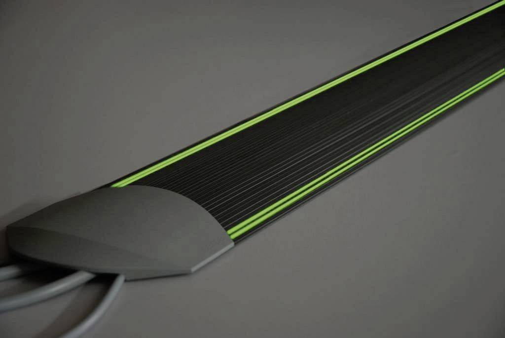 Sistema di gestione cavi nero lungo con strisce verdi, progettato per organizzare in modo sicuro e ordinato i cavi sul pavimento.