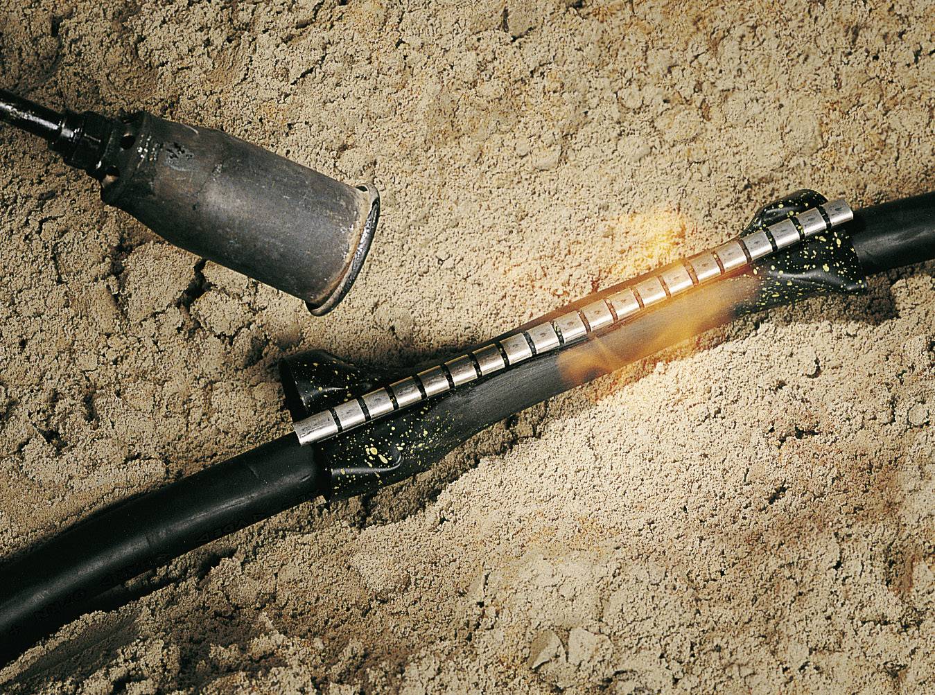 Un bruciatore ad aria calda viene utilizzato per fissare un elemento di giunzione termorestringente su un cavo che si trova nella sabbia.