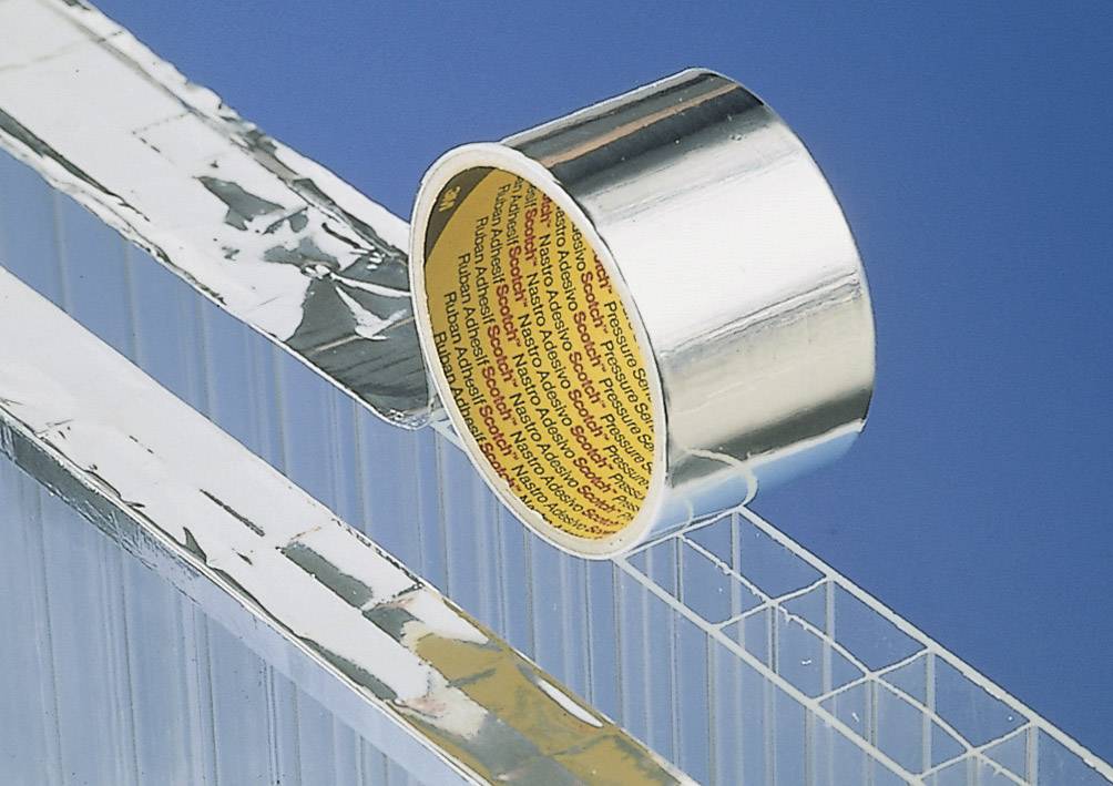 Un rotolo di nastro adesivo argentato è parzialmente srotolato su una superficie trasparente e strutturata con uno sfondo blu.