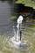 Gioco d'acqua in uno stagno con un getto d'acqua spumeggiante e pesci che nuotano, con foglie di ninfea sullo sfondo.