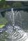 Una fontana da giardino spruzza l'acqua ad arco in uno stagno, circondato da ninfee e fogliame verde. La luce del sole si riflette sulla superficie dell'acqua.