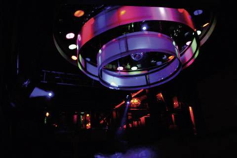 Una variopinta palla da discoteca illuminata pende in un locale dall'atmosfera cupa. Luci diverse si riflettono sulla pista da ballo.