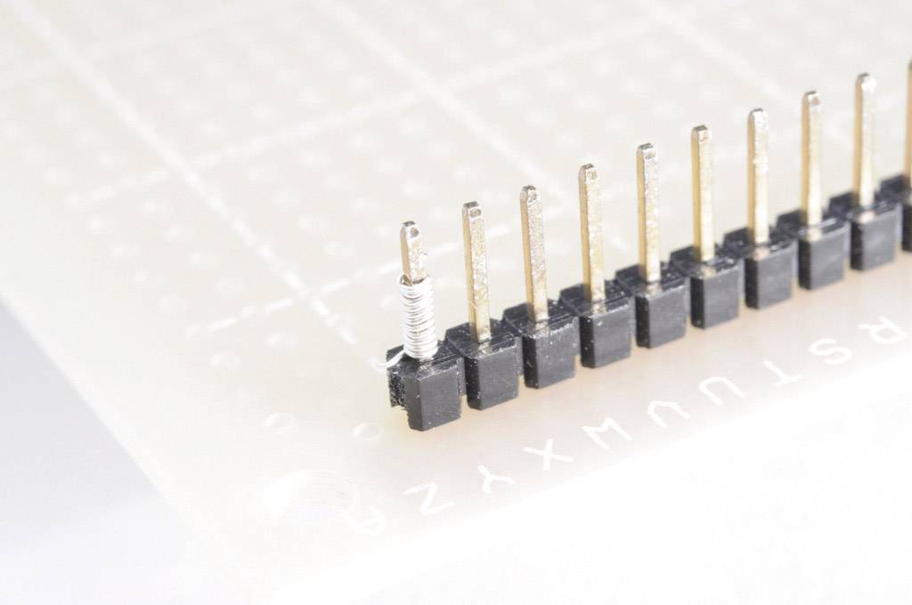 Una barra di pin nera a una fila è montata su una scheda PCB, con un avvolgimento di fili attorcigliato a sinistra su un pin.