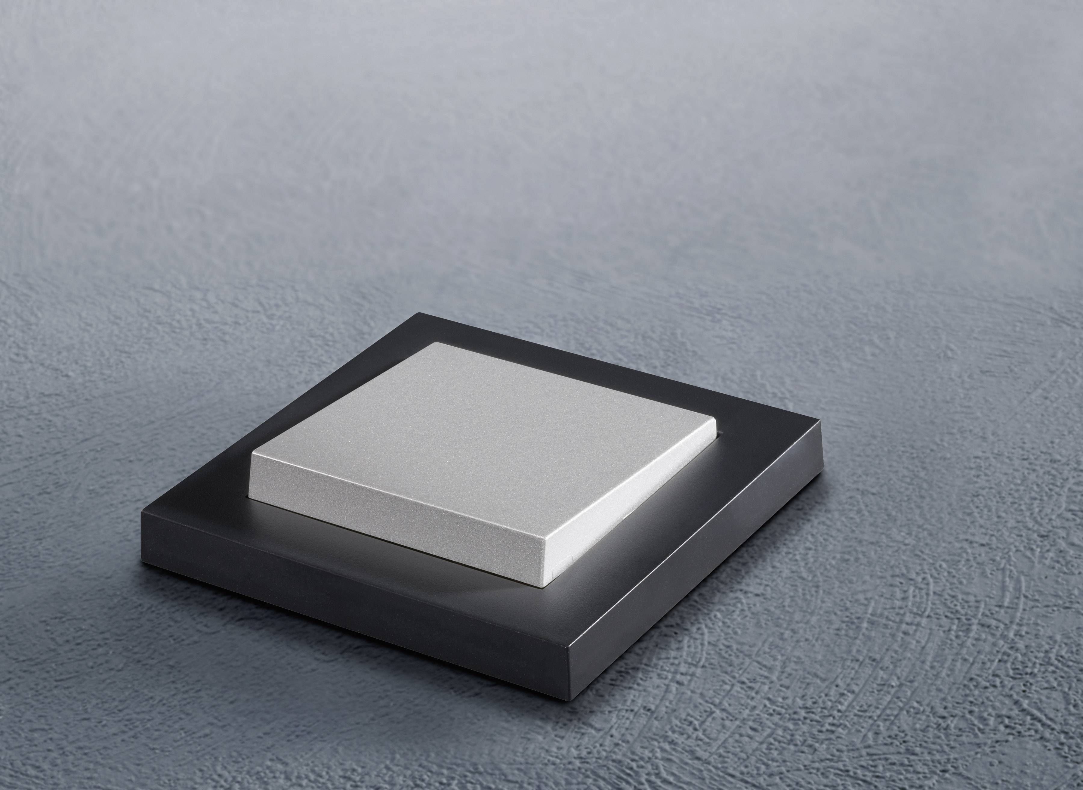 Un blocco quadrato d'argento poggia su un piedistallo quadrato nero su una struttura di superficie grigia.